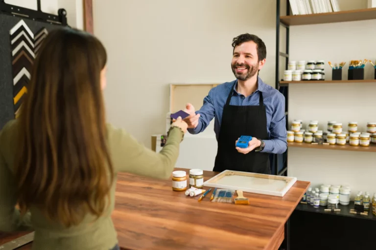 a-jovem-cliente-esta-entregando-ao-vendedor-sorridente-seu-cartao-de-credito-para-pagar-seus-suprimentos-de-arte-na-loja-pequenos-negocios-que-dao-certo-com-pouco-dinheiro