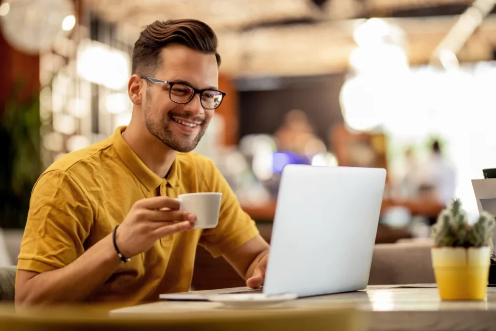 homem-sorridente-navegando-na-net-no-laptop-enquanto-bebe-cafe-quanto custa um domínio de site