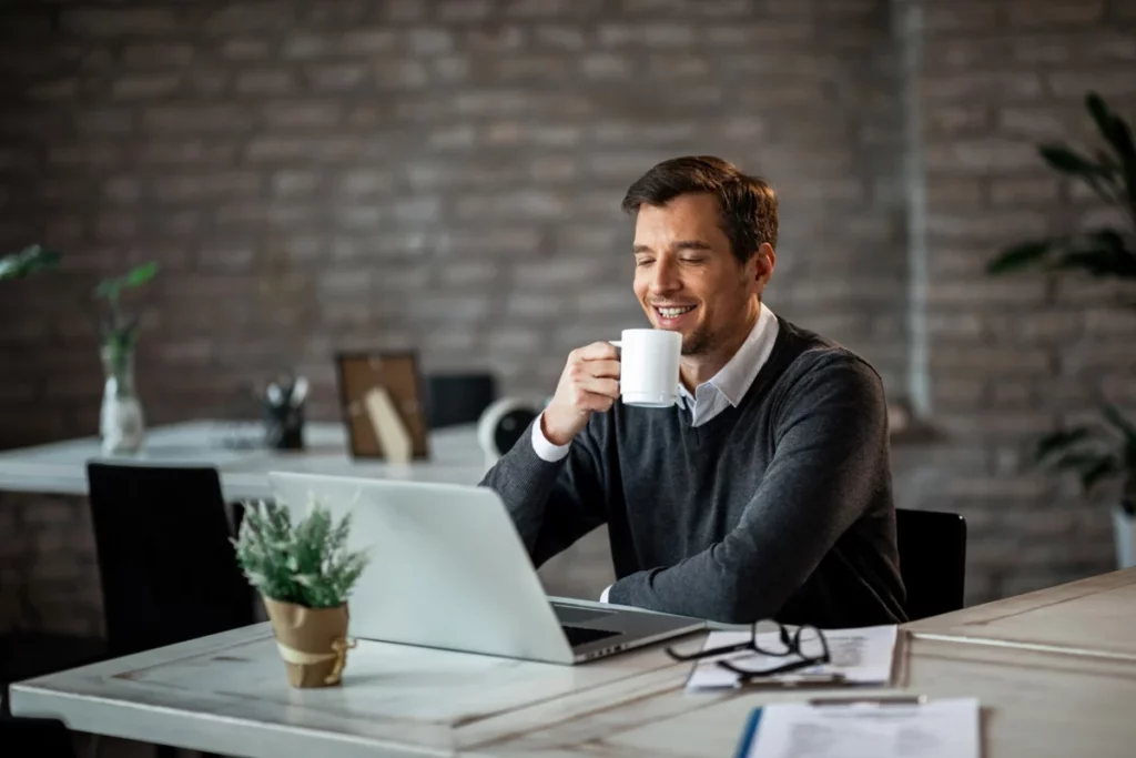 empreendedor feliz e bem vestido tomando café enquanto trabalha no computador em escritório - tipos de clientes