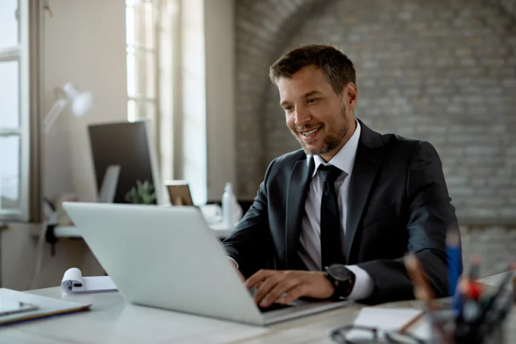 empreendedor feliz e bem vestido trabalhando no computador em escritório - o que precisa para abrir uma loja virtual