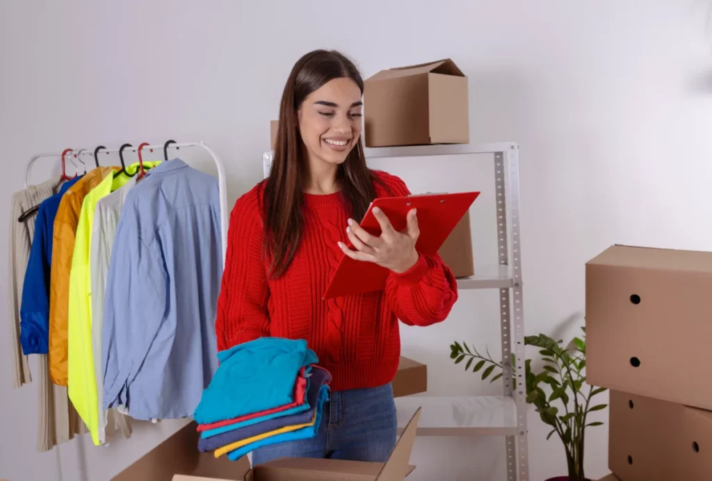 mulher de negócios conferindo prancheta e segurando roupas para venda - comprar no atacado para revender