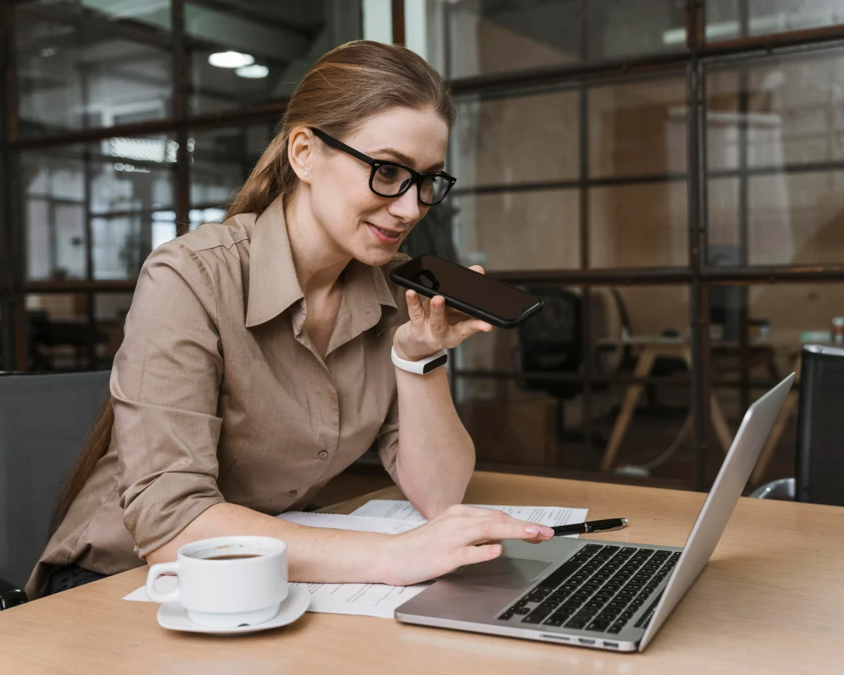 vista lateral de mulher falando ao celular de frente para o computador com café ao lado - plataforma de marketplace