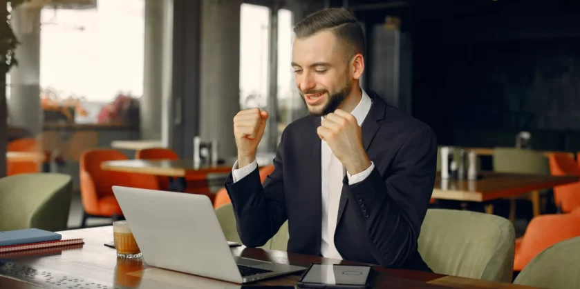 homem de negócios bem vestido comemorando em frente ao notebook - maiores marketplaces brasil