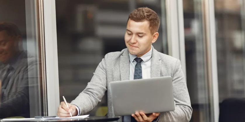 homem de negócios sentado ao ar livre mexendo no computador e anotando em papel - curso de marketplace