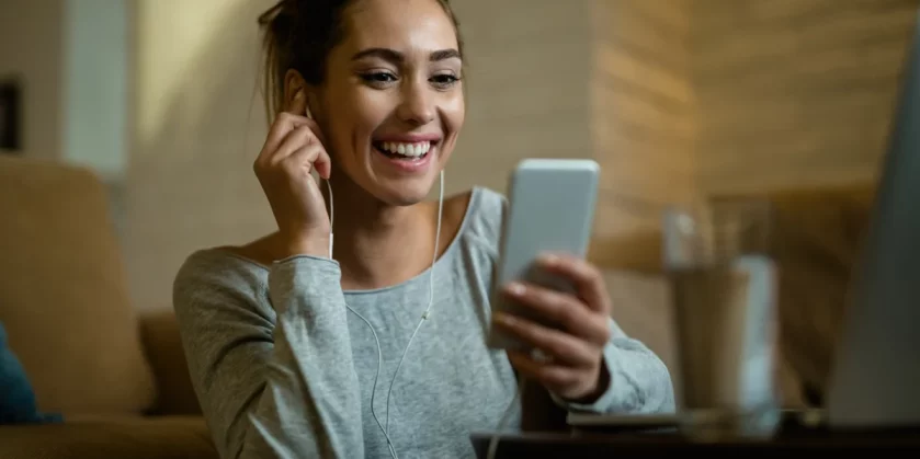 mulher-sorridente-olhando-para-o-celular-e-colocando-fones-de-ouvido-loja-de-produtos-eletronicos